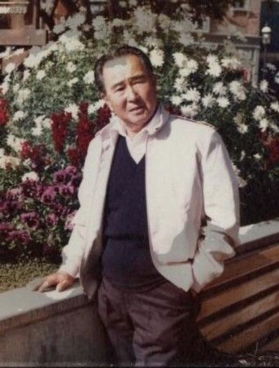 Masami in a light jacket poses in front of a background of flowers while traveling in Japan. Press Enter to Activate this item.