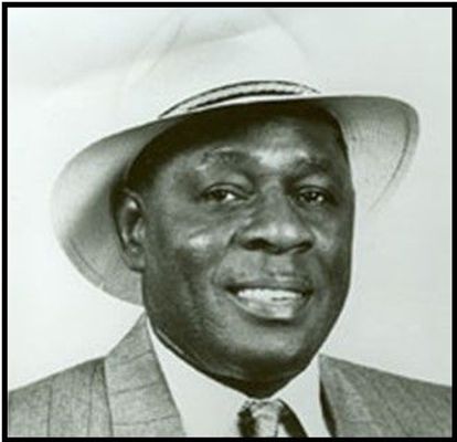 George Benton, smiling, wearing a jacket and tie and white hat.